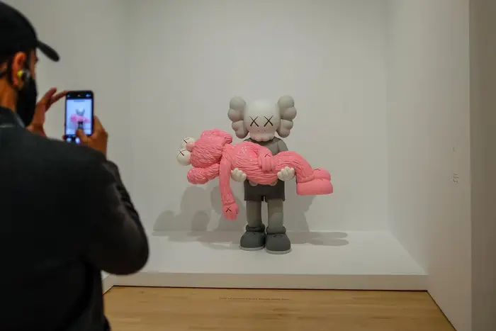 One sculpture carrying another pink sculpture. Inside the KAWS exhibit at Brooklyn Museum